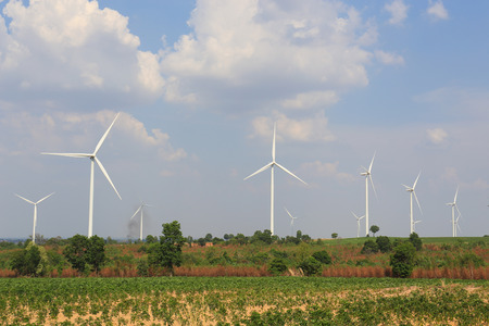 Wind turbine on the green grass over the blue clouded sky.