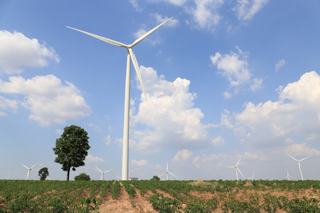 Wind turbine on the green grass over the blue clouded sky.
