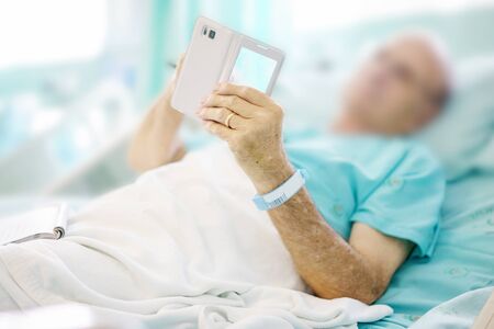 Mature male patient playing a mobile on bed in hospital.の写真素材