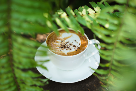 Cup of coffee cappuccino art on wood floor with green leave frame.の写真素材
