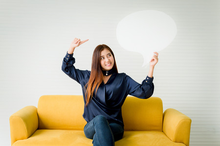 Beautiful woman holding a speech bubble on a yellow sofa.