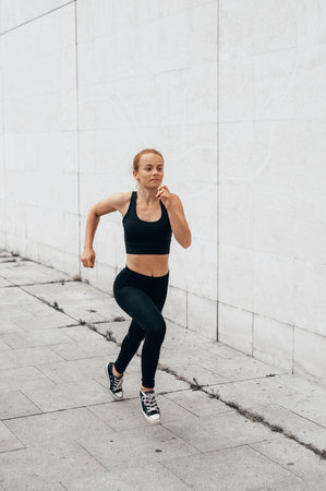 Young woman in black sportswear running through the city. vertical photo for social networksの写真素材