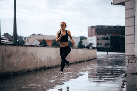 Beautiful fit girl outside run in the rain. Urban run, Pain while runningの写真素材
