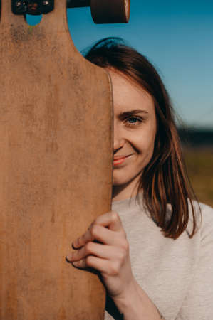 Portrait of a pretty girl holding a longboard in front of her face.の写真素材