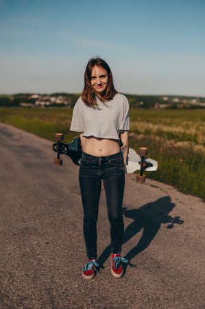 Portrait of a smiling girl holding a longboard behind her back. sunny day, longboard day, poster,...