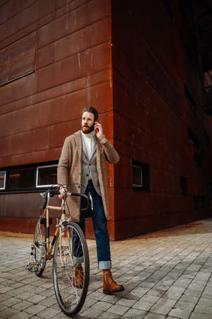 Young man with bicycle going to work. Calling with manager. Creative businessman in a modern business area.の写真素材