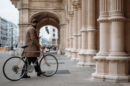 Young man holding smartphone and walking with bicycle. Eco friendly transport.の写真素材