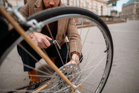 Man checking wheels on bike. Repairing bicycle at street.