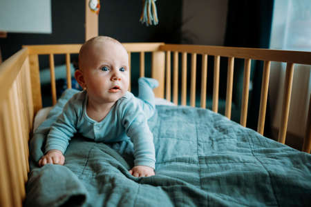 Baby boy toddler crawling in crib at kids nursery room at home. looking and smiling at the cameraの写真素材