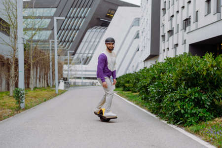 man in a helmet rides an electric skateboard. Onewheel rider in an urban background.