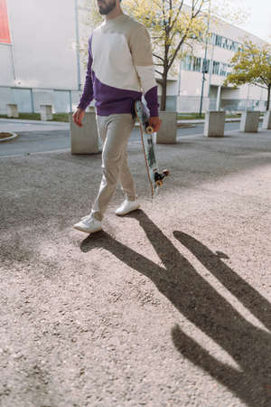 Midsection of skateboarder. Stylish cool man walking down the street. Urban spot. Vertical photo.
