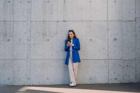 Woman using internet banking mobile app. Long shot. Standing in front of wall. Isolated background.