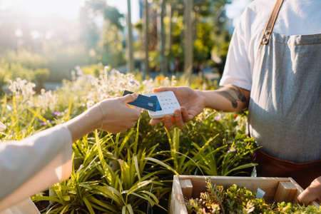 Woman customer is paying by credit card in garden centre. Money transaction.