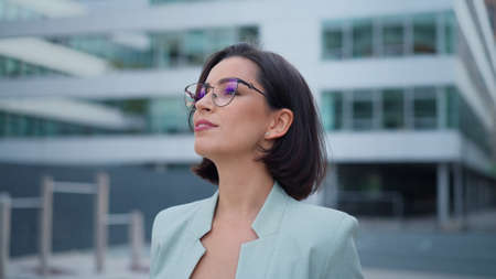 Front closeup portrait of young businesswoman with brown hair standing on street, looking friendly at cameraの写真素材