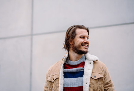 Smiling male model looking at the distance while posing over the blank wall
