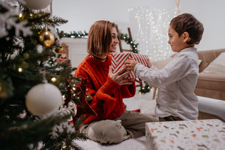 Lovely boy giving present to his mother under the Christmas treeの写真素材