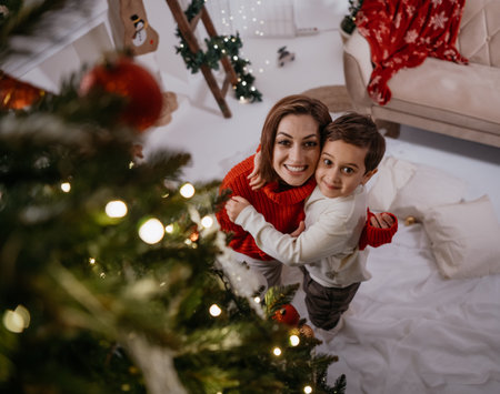 Single mother and her little son embracing and looking camera with pleasant smile at cozy homeの写真素材