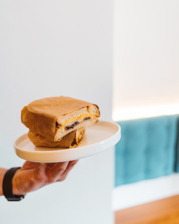 Unknown man hand holding fresh fried sandwich on white plate in restaurant. Breakfast conceptの写真素材