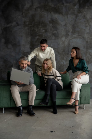 Vertical view of the focused colleagues sitting green sofa and looking at the computer at the officeの写真素材