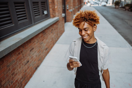 Multiracial guy teenage student using smartphone outdoor on city street while walking aloneの写真素材