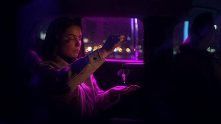 Serious business woman holding and examining amethyst crystal on silver chain at neon light