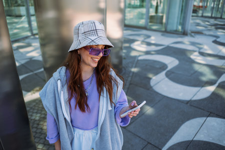Pretty woman in good mood on city street while listening and scrolling music from her smartphoneの写真素材