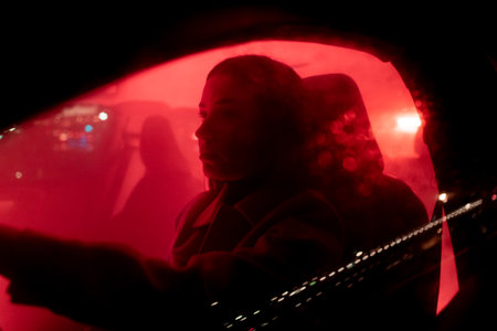 Serious businesswoman enjoying night drive while driving the red light background car
