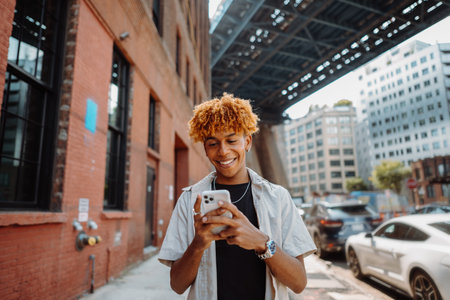Young handsome guy walks across the street, typing messages on a smartphone and smilingの写真素材