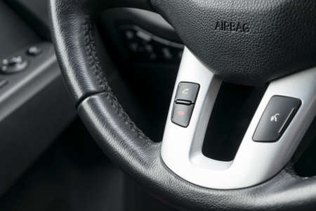 Hands free and media control buttons on the steering wheel in black leather, modern car interior