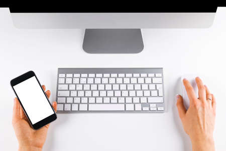 businesswoman hand holding phone on workplace with computer mouse and keyboard, space for textの写真素材