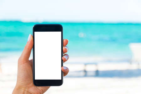 Beautiful woman's hand using smart phone at beach. Smartphone white screen.Blank empty screenの写真素材
