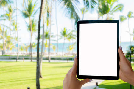 Beautiful woman's hand using tablet computer at beach. Tablet computer white screen. Blank empty...