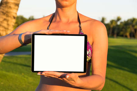 Attractive young outdoor bikini girl holds the tablet computer. blank empty screen, space for text, white screenの写真素材