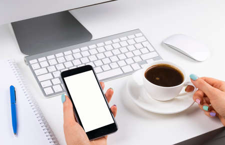 Woman hands holding the phone with isolated screen and cup of coffee. Business workplace with...