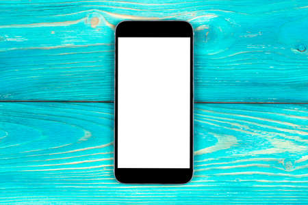 Mobile phone with blank screen mock up isolated on blue wood table background. Smartphone on wood...