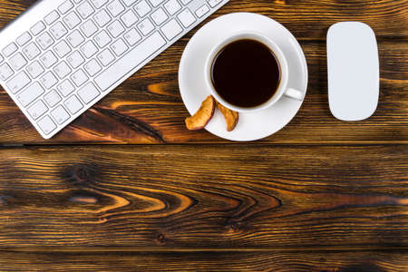 Office desk with copy space. Digital devices wireless keyboard and mouse on burned wooden table with cup of coffee, top viewの写真素材