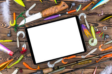 Fishing rod, tackles and fishing baits, reel on wooden board background with tablet computer isolated white screen, empty space for textの写真素材