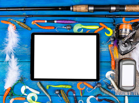 Fishing rod, tackles and fishing baits, reel on wooden board background with tablet computer isolated white screen, empty space for textの写真素材