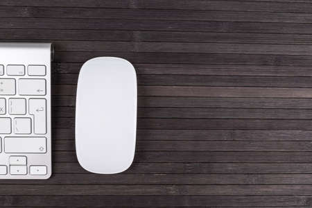 Close up view of a business workplace with wireless computer keyboard, keys and mouse on old dark wooden table background.  Office desk with copy spaceの写真素材
