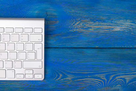 Business workplace with  wireless keyboard on old blue wooden table background. Office desk with copy spaceの写真素材