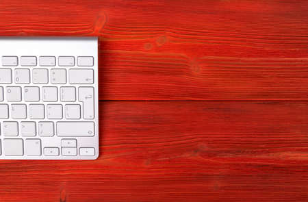 Close up view of a business workplace with wireless computer keyboard, keys on old red natural wooden table background. Office desk with copy spaceの写真素材