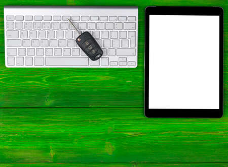 Business Workplace with wireless keyboard, tablet computer and car keys on green wooden background....