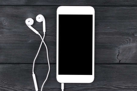 Smartphone with headphones on black wooden table. Smartphone with isolated screen. Empty space for text. Copy space. Smartphone blank screen. Smartphone mock up. earphone.の写真素材