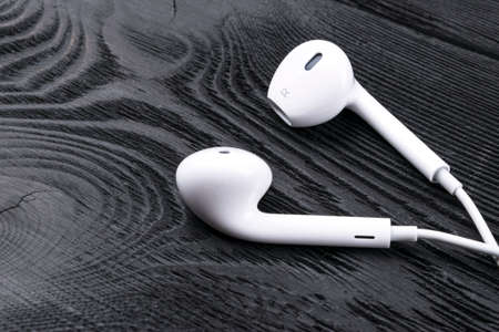 White little headphones on a black rustic wooden isolated background, woodgrain textureの写真素材