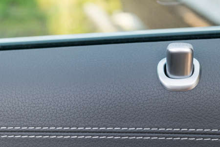 Door handle with lock contol buttons of a luxury passenger car. Black leather interior of the luxury...