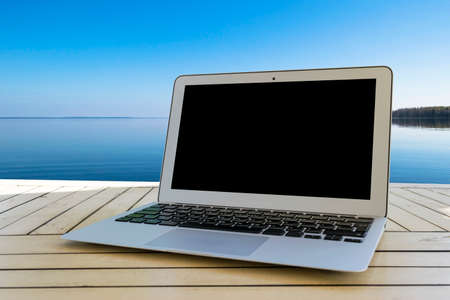 Laptop computer on wooden table. Front ocean view. Tropical island background. Open blank laptop computer empty space. Front view with copy space.の写真素材