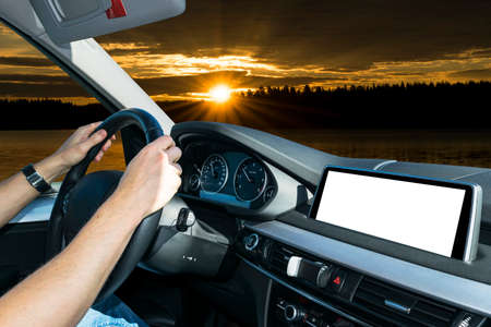 Male hands holding car steering wheel. Hands on steering wheel of a car driving near palm field. Man driving a car inside cabin. Multimedia system isolated white blank screen. Copy spaceの写真素材