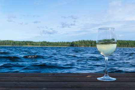Glass of wine at a wooden pier.  Luxury resort vacation concept. Blue Lake and  green forest background.の写真素材