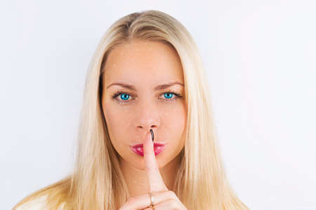 Shh! Women's secrets. Beautiful blond Woman with blue eyes holding her finger to her pink lips in a...