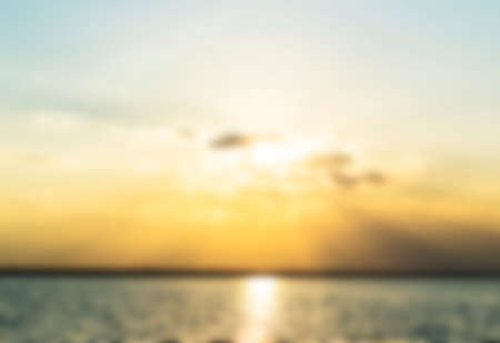Blurred Sunset over the ocean through clouds, blur gold sun, sea and skyの写真素材